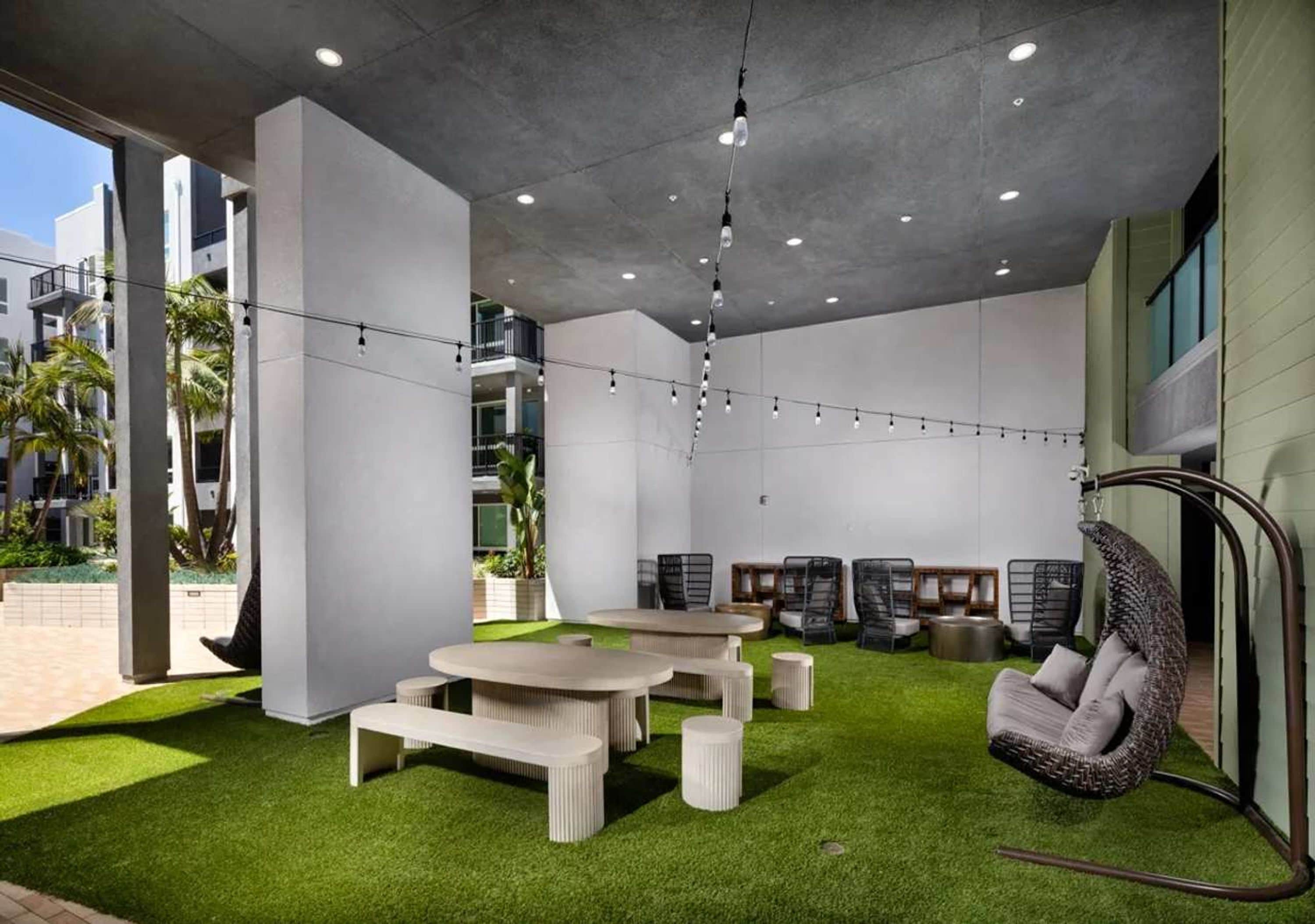 Un espace intérieur doté d’un plafond en béton, d’un revêtement de sol en gazon synthétique, d’une chaise suspendue et d’une table avec des bancs.