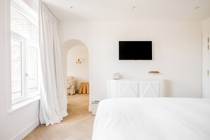 Un dormitorio moderno con una cama grande, un televisor de pantalla plana montado en la pared y una ventana con cortinas blancas.