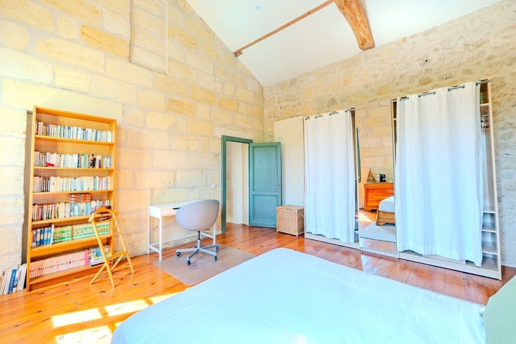 A room with a large bed, a bookshelf, a desk, and a wardrobe with sliding doors.