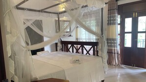 Una habitación con una cama bajo un dosel, un banco de madera y una puerta con cortinas estampadas.