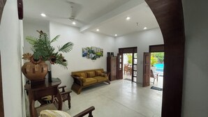 Un salón amplio con sofá, una mesita de centro y una planta en maceta. Hay una puerta que da a un espacio exterior con piscina.