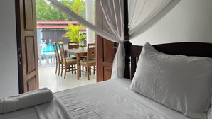 Un dormitorio con cama, una mesa, sillas y vistas a una piscina y follaje exterior.