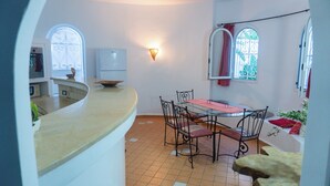 A kitchen with a curved countertop, a dining table with chairs, and a window with curtains.