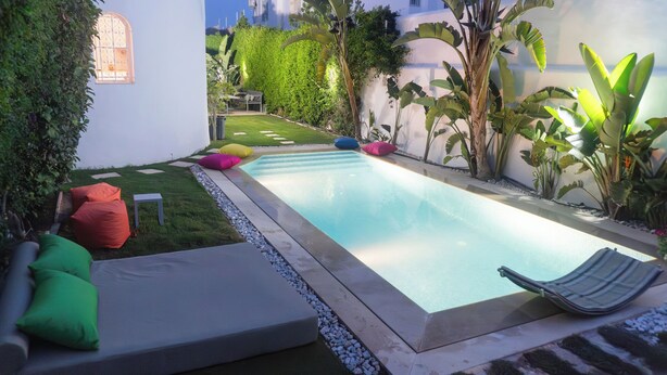 A rectangular swimming pool with a surrounding deck, a lounge chair, and colorful cushions.