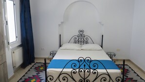 A bedroom with a bed, a window with curtains, a radiator, and a wall-mounted air conditioner.