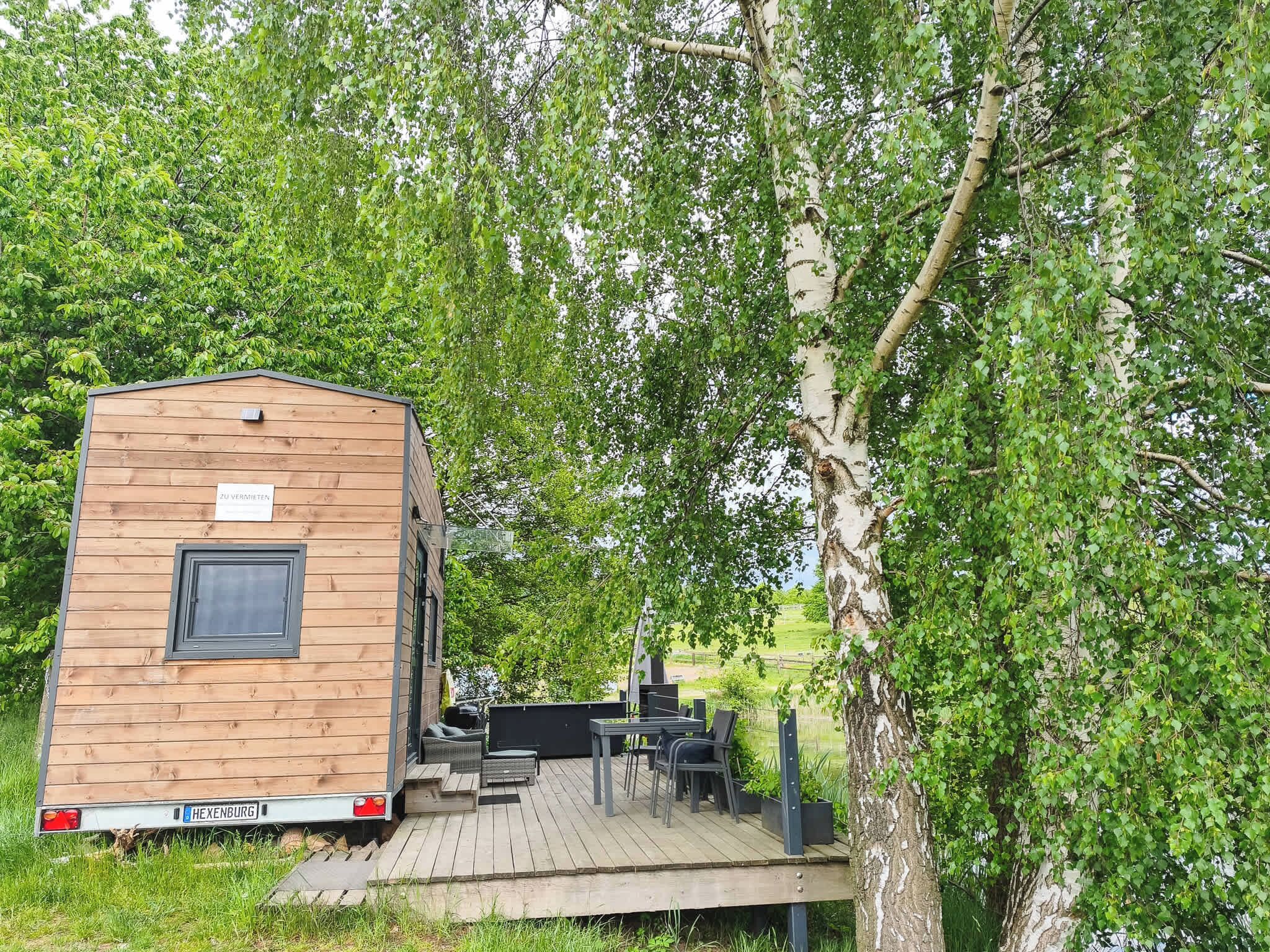 Eine Holzhütte mit einer Terrasse, Gartenmöbeln und einem Schild mit der Aufschrift 'ZU VERMIETEN'.