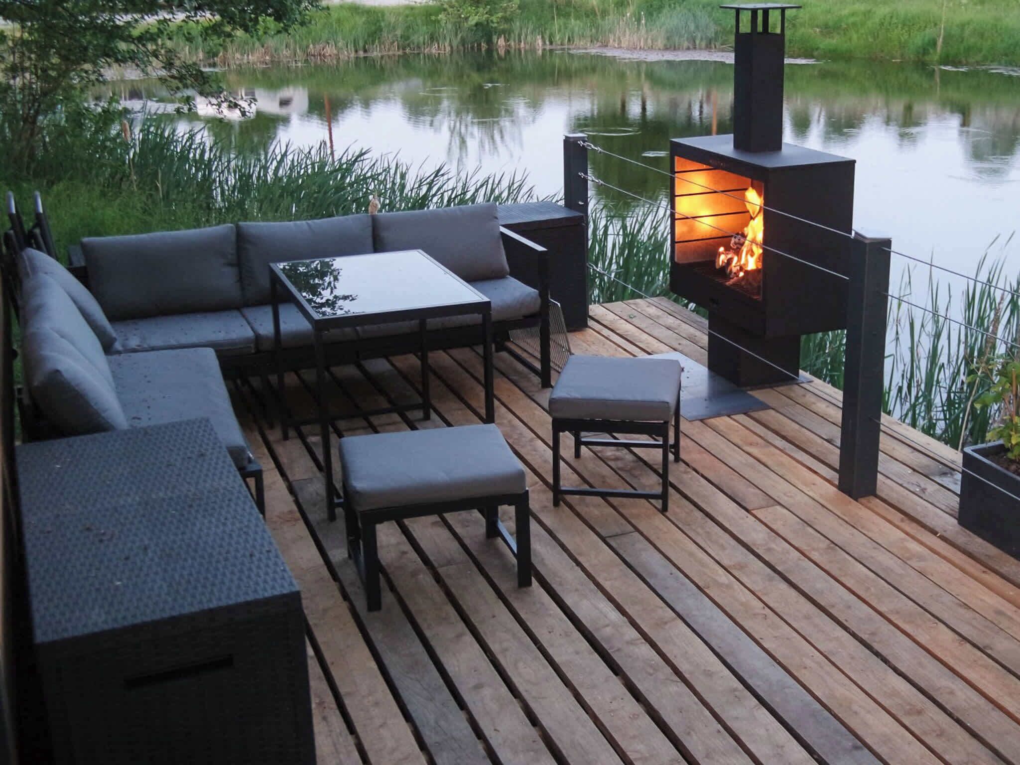 Une terrasse extérieure dotée d’un foyer, de sièges et offrant une vue sur un plan d’eau.