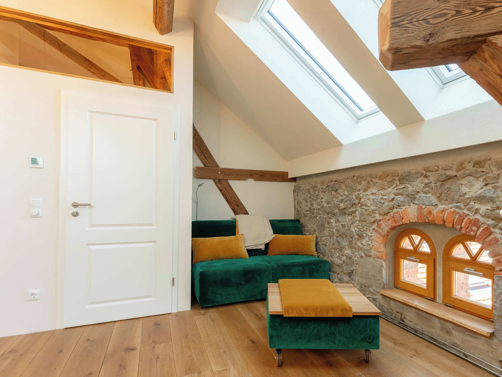 A loft-style room with a skylight, stone wall, and a green sofa with cushions.