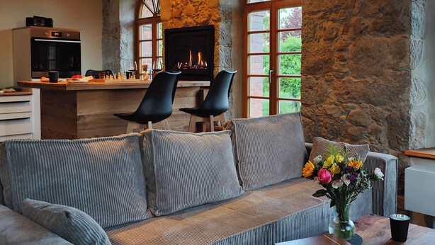 A cozy living area with a stone wall, a fireplace, a sofa, and a dining table. - Private sauna, 2 fireplaces: Bright flat - last minute (Großharthau)