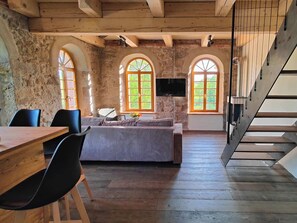 Una habitación rústica con una mesa de madera, sillas, un sofá, un televisor y ventanas de arco.
