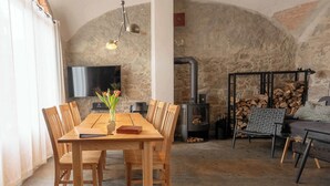 A dining area with a wooden table and chairs, a vase with flowers, a fireplace, and a stone wall. - Two-storey accommodation with terrace and fireplace – last minute (Großharthau)