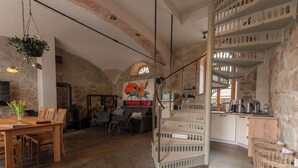 A rustic interior with exposed stone walls, a wooden dining table, a sofa, and a kitchen area with white cabinets and a hanging basket. - Two-storey accommodation with terrace and fireplace – last minute (Großharthau)