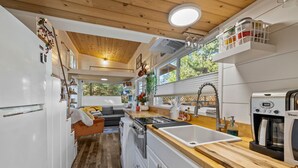 A compact kitchen with white cabinets, a wooden countertop, a built-in oven, and a window overlooking greenery.