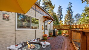 An outdoor deck with a dining table set for two, surrounded by a wooden fence and trees.