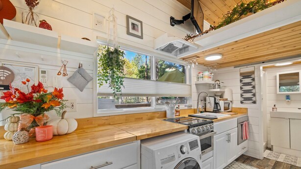 A modern kitchen with wooden countertops, a built-in washing machine, and a large window providing natural light.