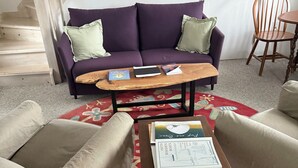 Een woonkamer met een paarse bank, twee fauteuils, een salontafel en een rood vloerkleed met een patroon.