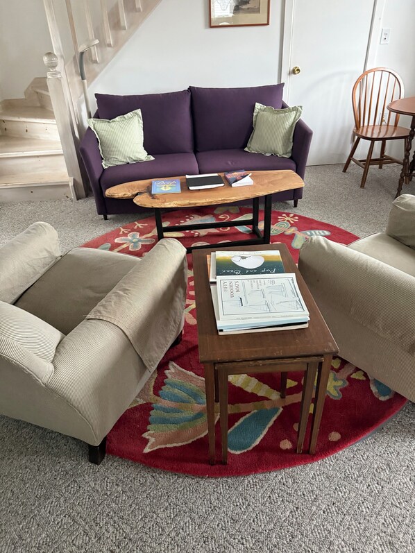 A living room with a purple sofa, two armchairs, a coffee table, and a red patterned rug. - Historic waterfront cottage offers quiet, comfortable intimacy. (Frenchboro)
