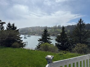 A river with boats, surrounded by trees and a grassy area. - Historic waterfront cottage offers quiet, comfortable intimacy. (Frenchboro)