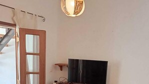 Una habitación con una cama de madera, un televisor sobre un mueble de madera, un escritorio de madera y una puerta con paneles de vidrio.