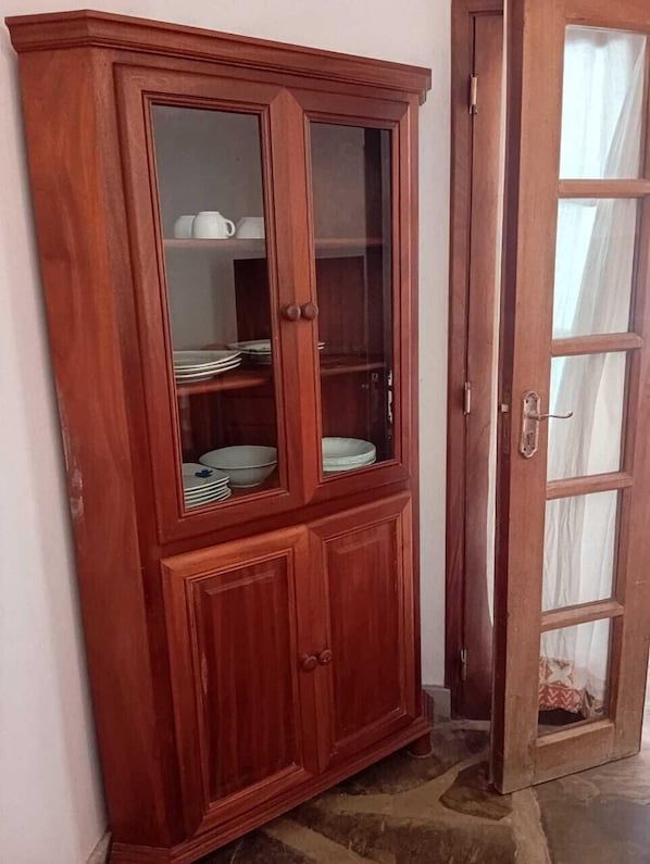 A wooden cabinet with glass doors, containing stacked plates and bowls.