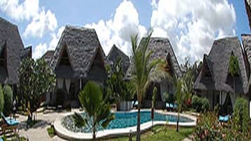 Un resort con cottage a tetto di paglia, una piscina e lettini da relax.