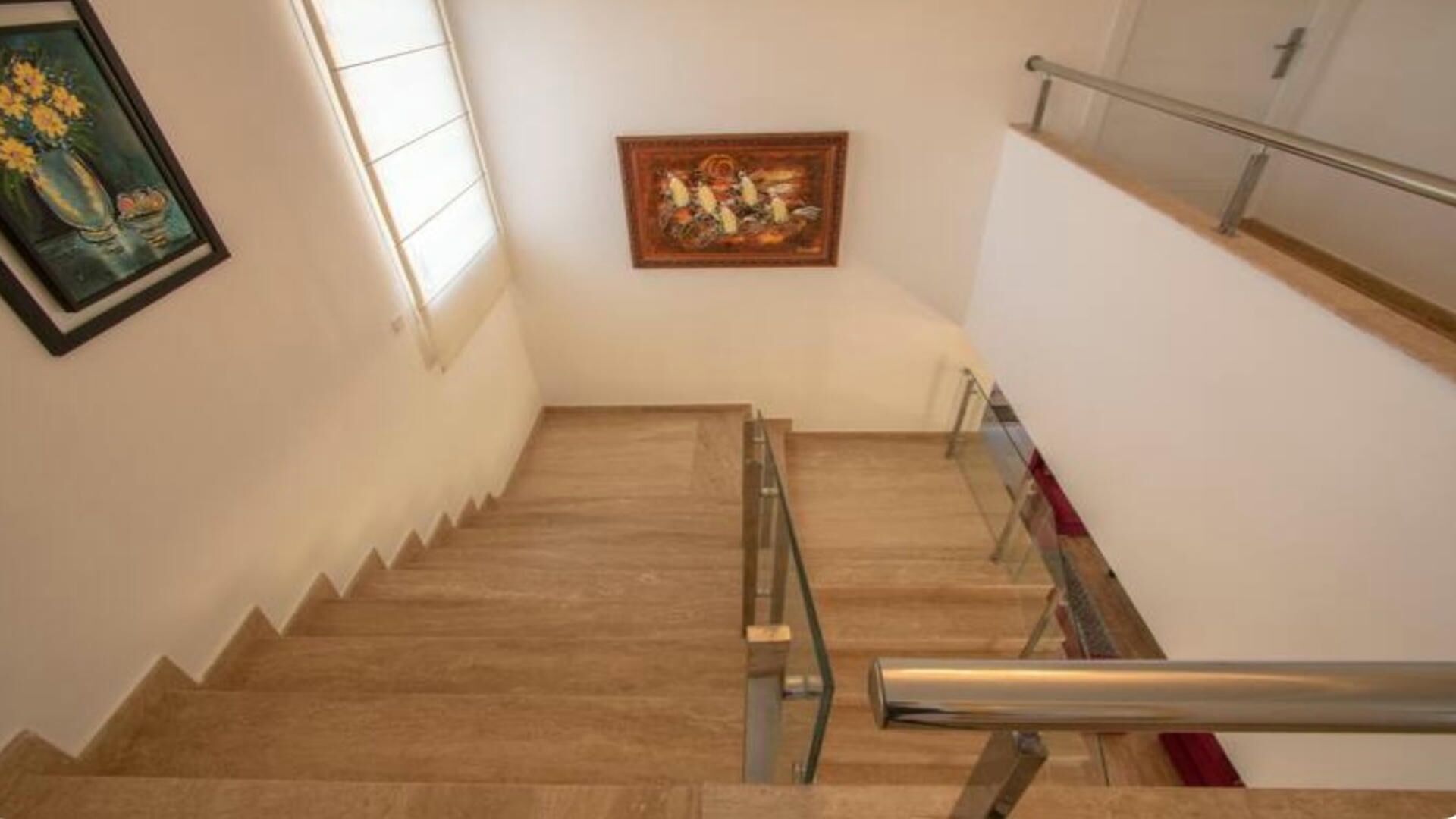 A staircase with wooden steps and metal handrails, leading to a landing with a framed painting.