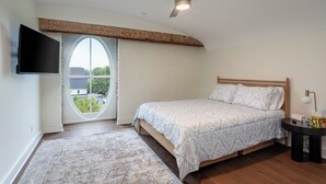 Ein Schlafzimmer mit einem Bett, einem Nachttisch, einer Lampe, einem Deckenventilator und einem an der Wand montierten Fernseher.