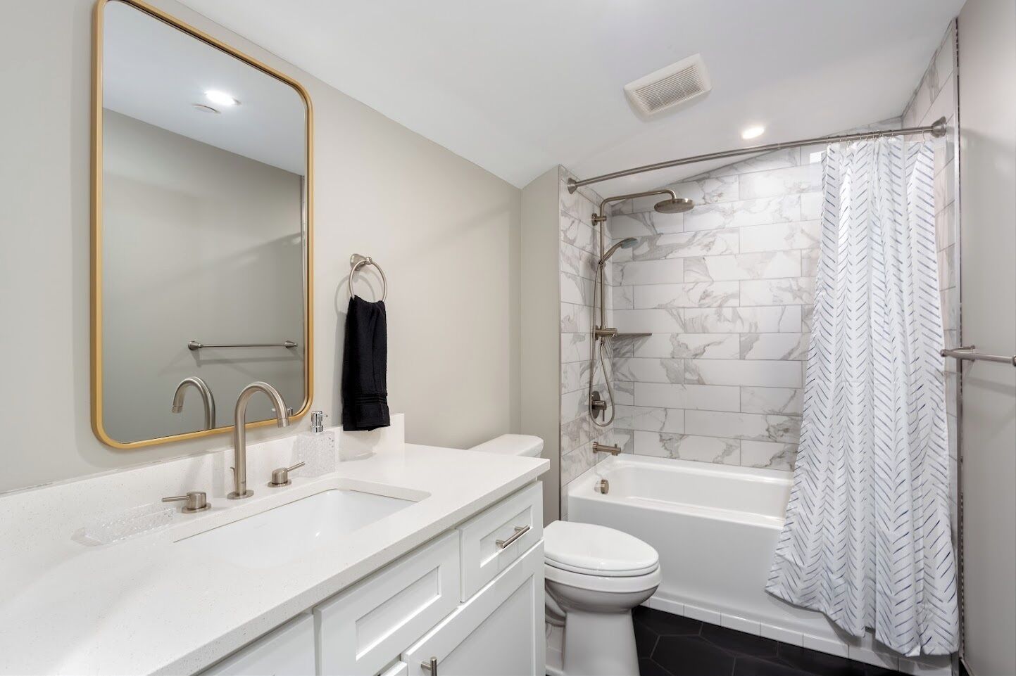 A modern bathroom with a large mirror, two sinks, a toilet, and a walk-in shower with a herringbone-patterned tile wall.