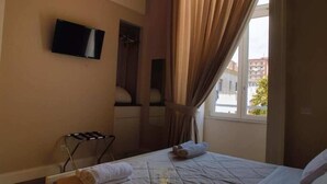 Ein Hotelzimmer mit einem Bett, einem an der Wand befestigten Fernseher, einem Fenster mit Vorhängen und einem Handtuchhalter.