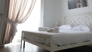 Une chambre à coucher avec un lit, une fenêtre avec des rideaux, un tableau au mur et un plafond orné d’un motif décoratif.