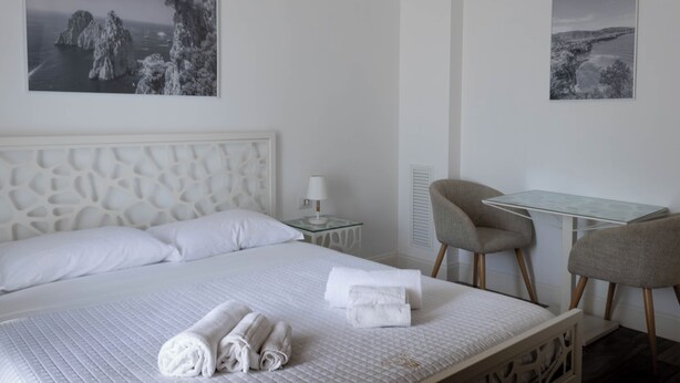 Une chambre d’hôtel avec un lit, deux chaises, une petite table et deux tableaux encadrés au mur.