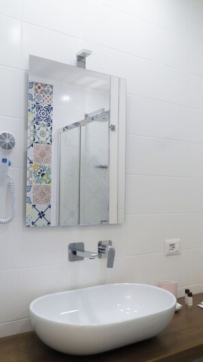 Un baño con lavamanos blanco, un espejo y un secador de pelo en la pared.