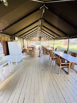 Un espace repas intérieur avec des tables et des chaises, un réfrigérateur blanc et un ventilateur de plafond.