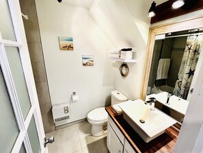 Une salle de bain avec des toilettes, un lavabo et une douche. On y trouve des serviettes et une petite étagère avec des articles de toilette.