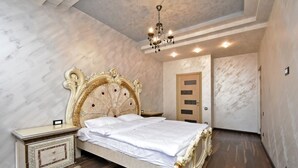 A bedroom with a large ornate bed, a nightstand, a chandelier, and a wooden door. - North Ave. apartment by Luxe Group HH777 (Yerevan)