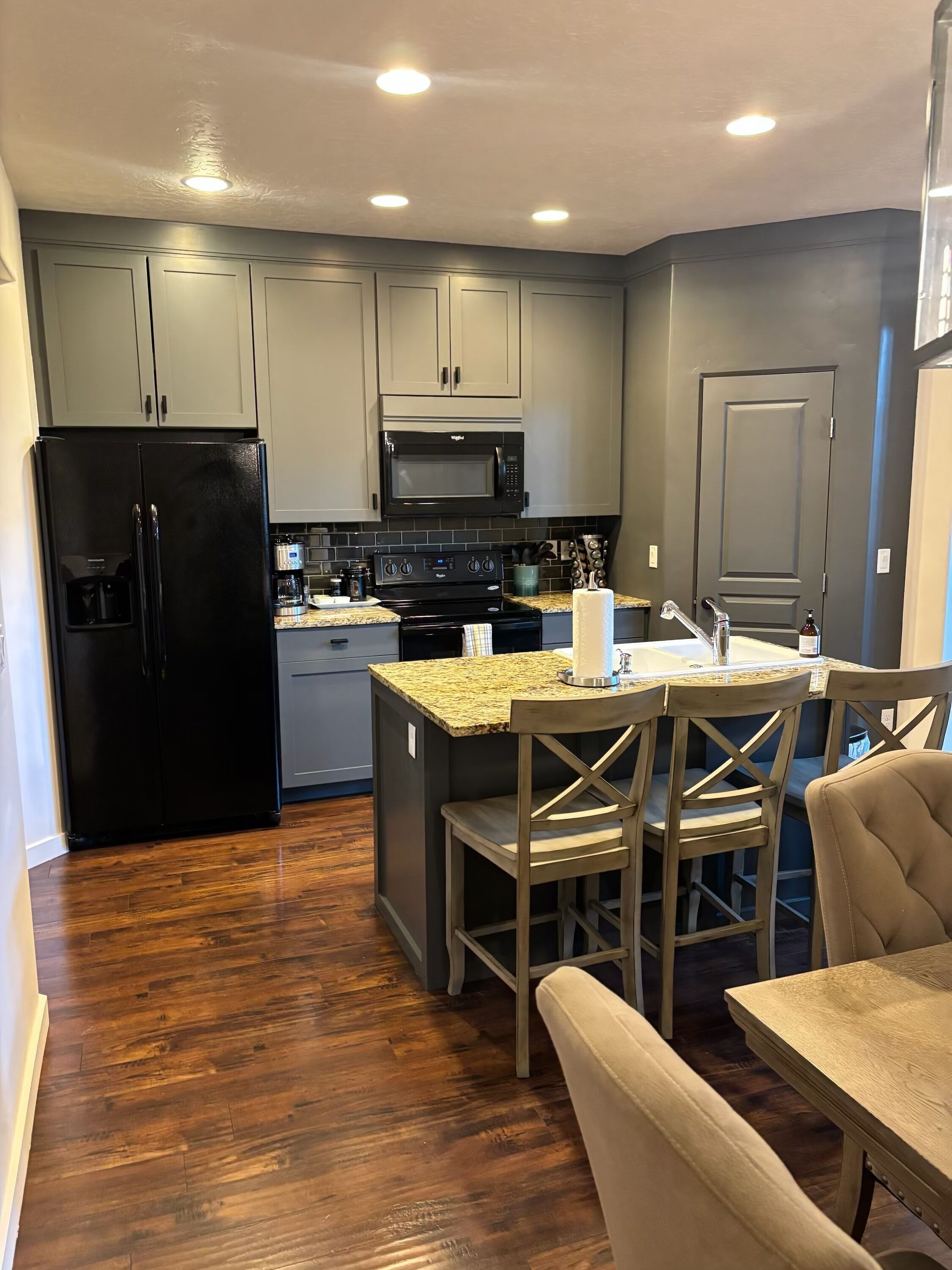 Una cocina moderna con armarios grises, un refrigerador negro, un microondas y una mesa de comedor de madera con sillas.
