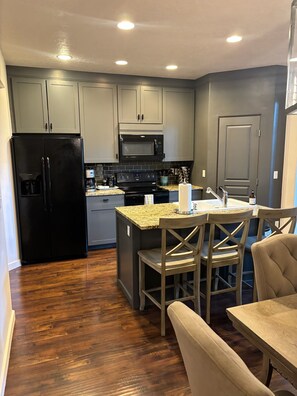 A modern kitchen with grey cabinets, a black refrigerator, a microwave, and a wooden dining table with chairs.
