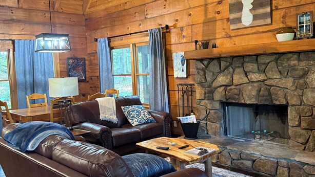 A cozy log cabin interior with a stone fireplace, leather sofas, and a dining area. - Rustic Log Cabin- In Town Cashiers- Pet-Friendly! (Cashiers)
