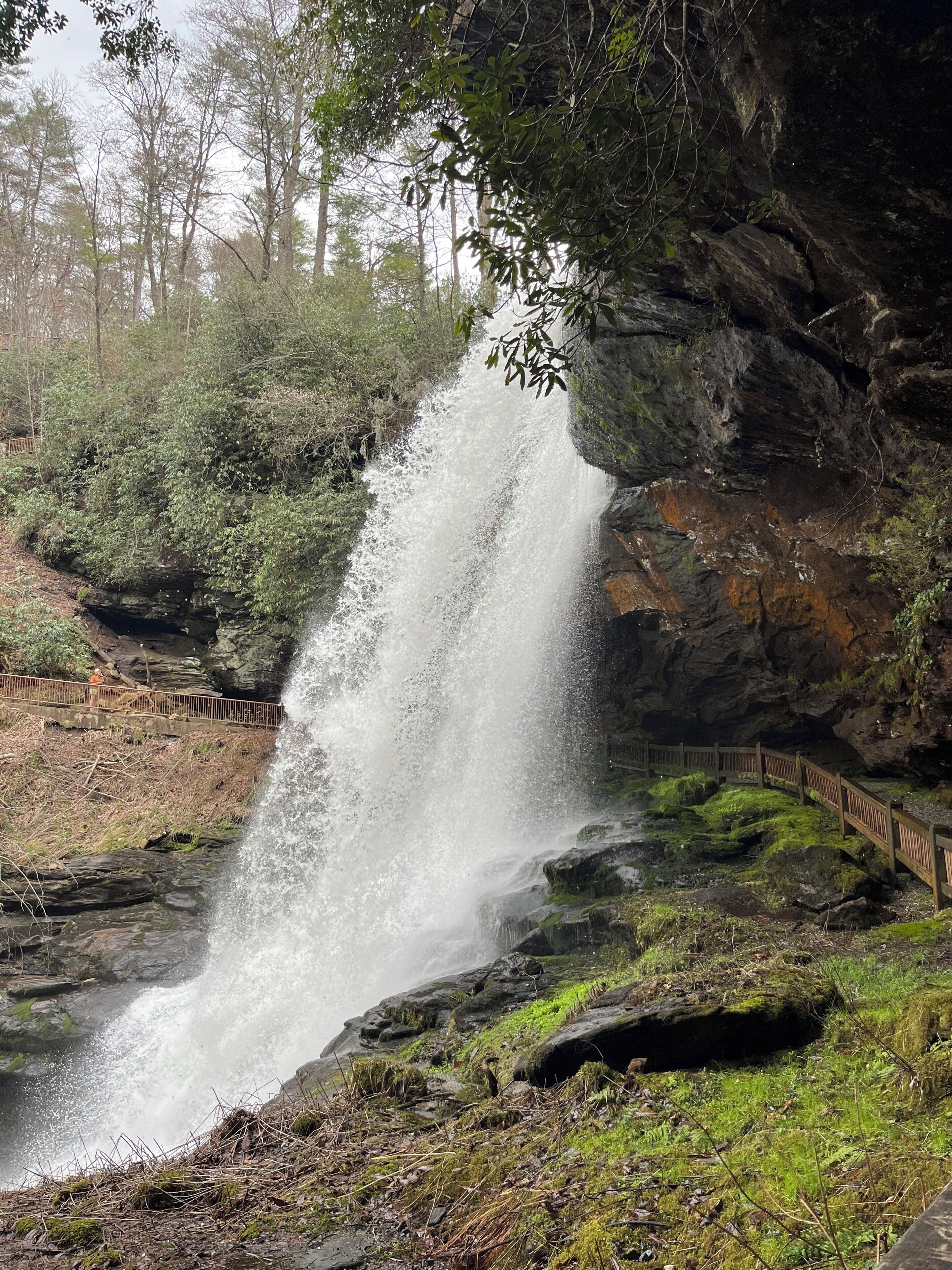 A waterfall cascading over rocks, surrounded by greenery and a wooden walkway.