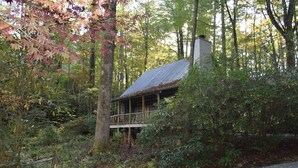 A rustic cabin with a wooden deck, surrounded by dense forest. - Rustic Log Cabin- In Town Cashiers- Pet-Friendly! (Cashiers)