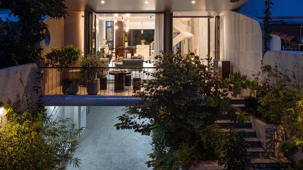A modern two-story house with a circular glass facade, a balcony with plants, and a well-lit interior.