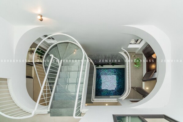 A modern interior with a spiral staircase, a large window with a mosaic pattern, and a kitchen area.