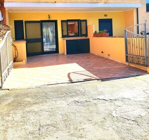 A building with a yellow facade, black shutters, and a tiled patio area.