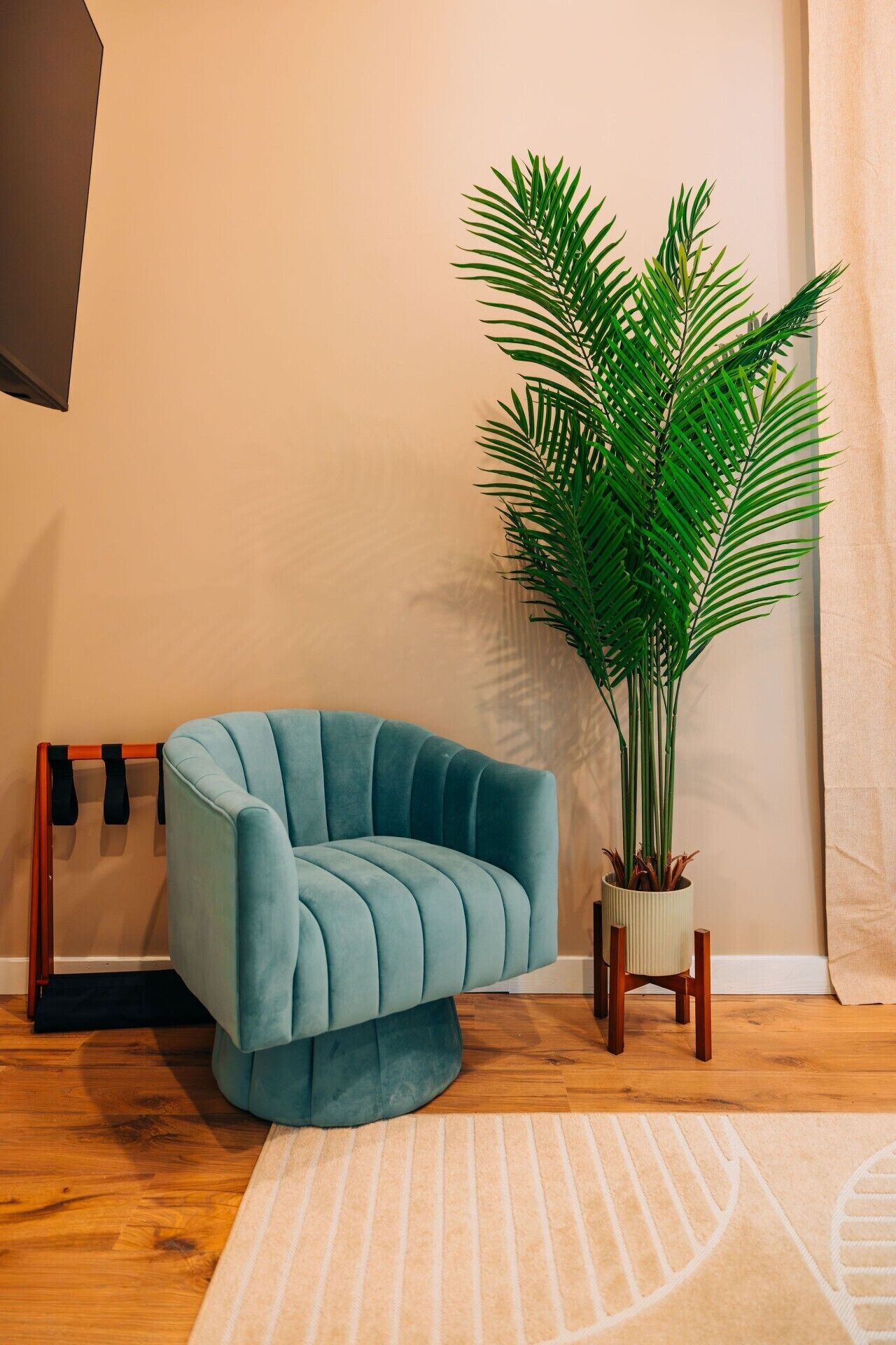 Un fauteuil de couleur bleu-vert avec un piétement en bois, une plante en pot aux longues feuilles vertes et un tapis à rayures posé sur un plancher en bois.