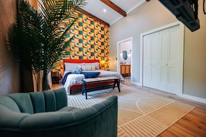 A bedroom with a patterned wall, a bed, a bench, and a large plant.