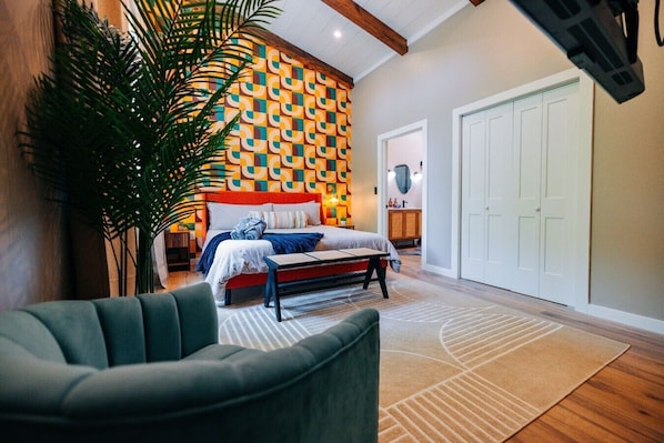 Un dormitorio con pared estampada, una cama, un banco y una planta grande.
