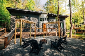A cabin with a deck, outdoor seating, and a fire pit.