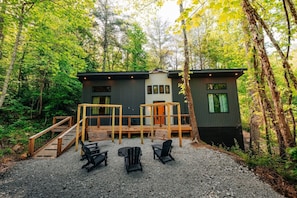 A cabin with a deck, outdoor seating, and a forest backdrop.