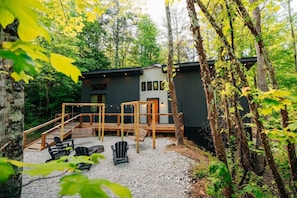 A cabin with a deck, outdoor seating, and a forest backdrop.