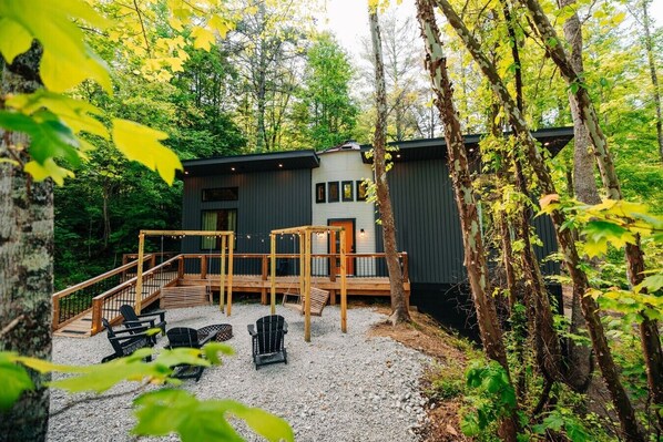 Una cabaña con terraza, mobiliario exterior y un bosque al fondo.